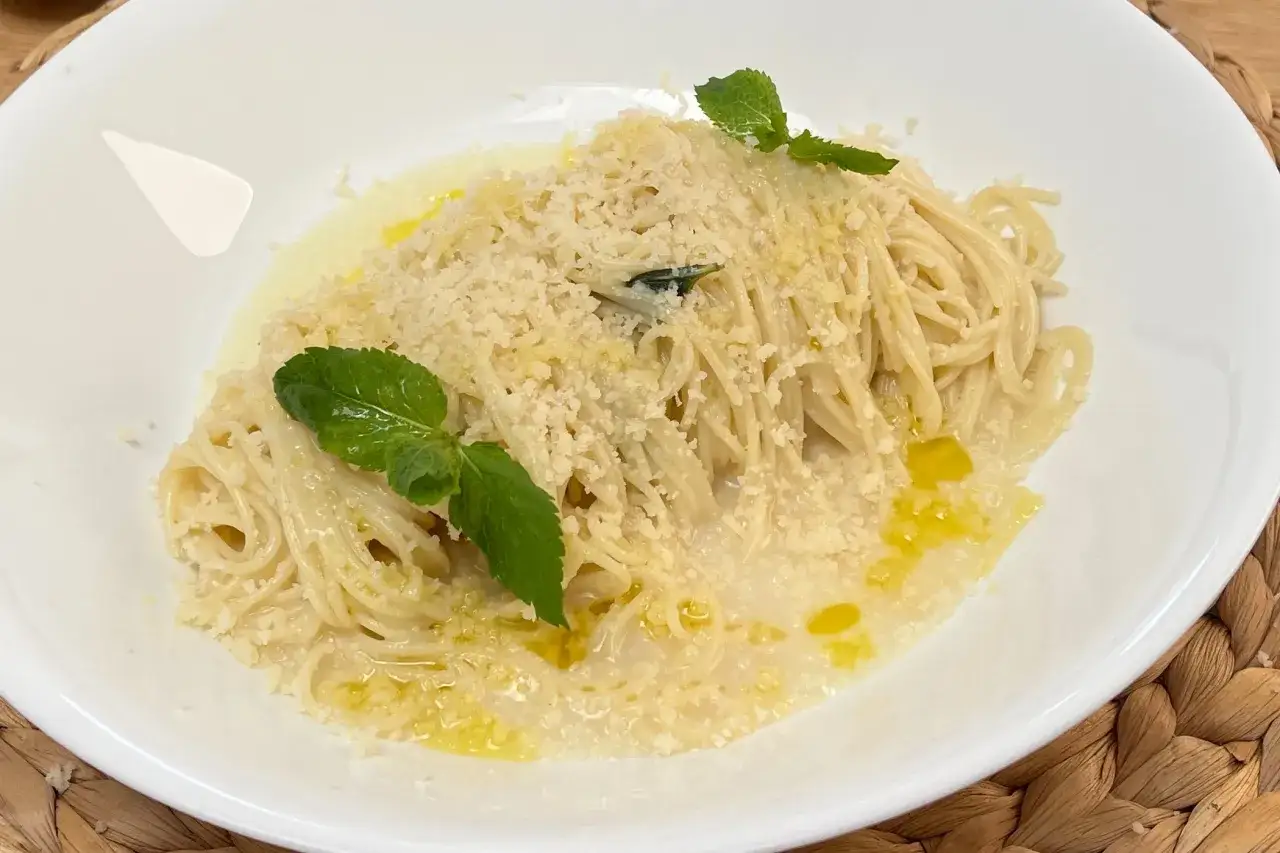 Spaghetti al limone cremosi, conditi con parmigiano e guarniti con foglie di menta fresca. Un piatto invitante e profumato.