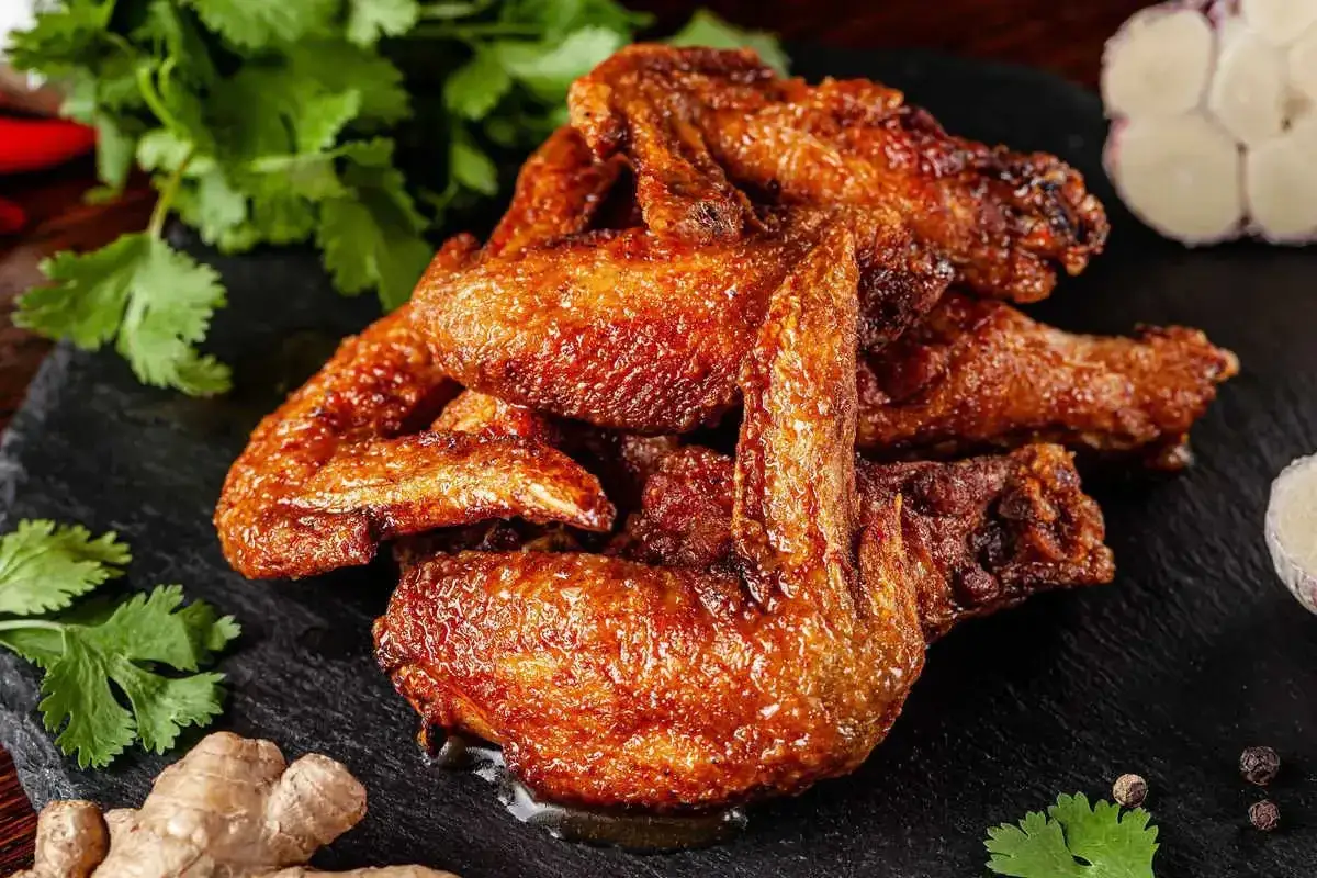 Alette di pollo al forno dorate e succulente, servite su una pietra scura con coriandolo, zenzero e aglio.