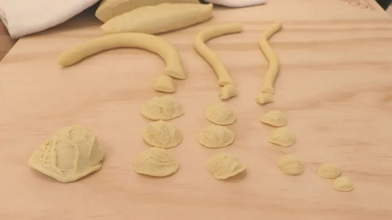 Orecchiette fatte in casa in lavorazione su un tagliere di legno. Strisce di pasta vengono tagliate e modellate.