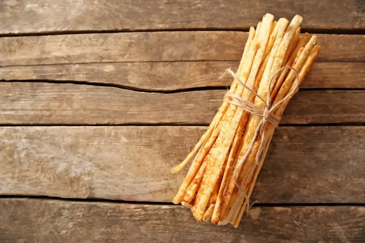 Un mazzo di grissini fatti in casa, dorati e croccanti, legati con spago su un tavolo di legno rustico.