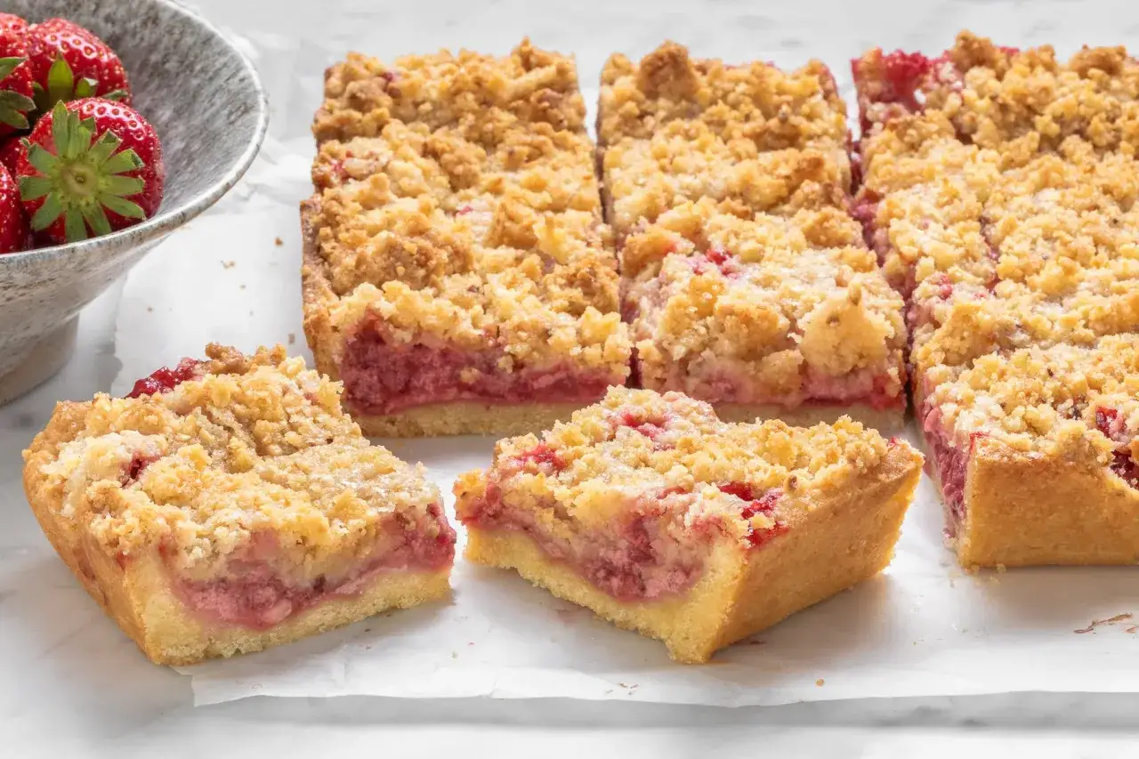 Fette di sbriciolata alle fragole, con la crosta dorata e il ripieno succoso, accanto a una ciotola di fragole fresche.
