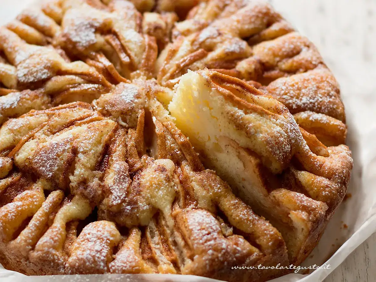 Una deliziosa torta di mele, cosparsa di zucchero a velo, con una fetta sollevata che mostra la morbida consistenza.