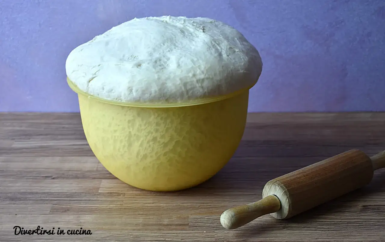 Impasto pizza bimby lievitato in ciotola gialla, pronto per essere steso con il mattarello.