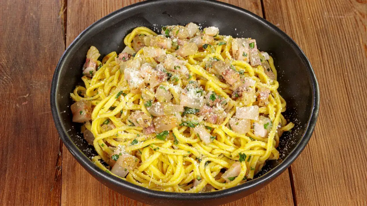 Spaghetti alla chitarra conditi con guanciale croccante, pecorino e prezzemolo, un piatto ricco e saporito.