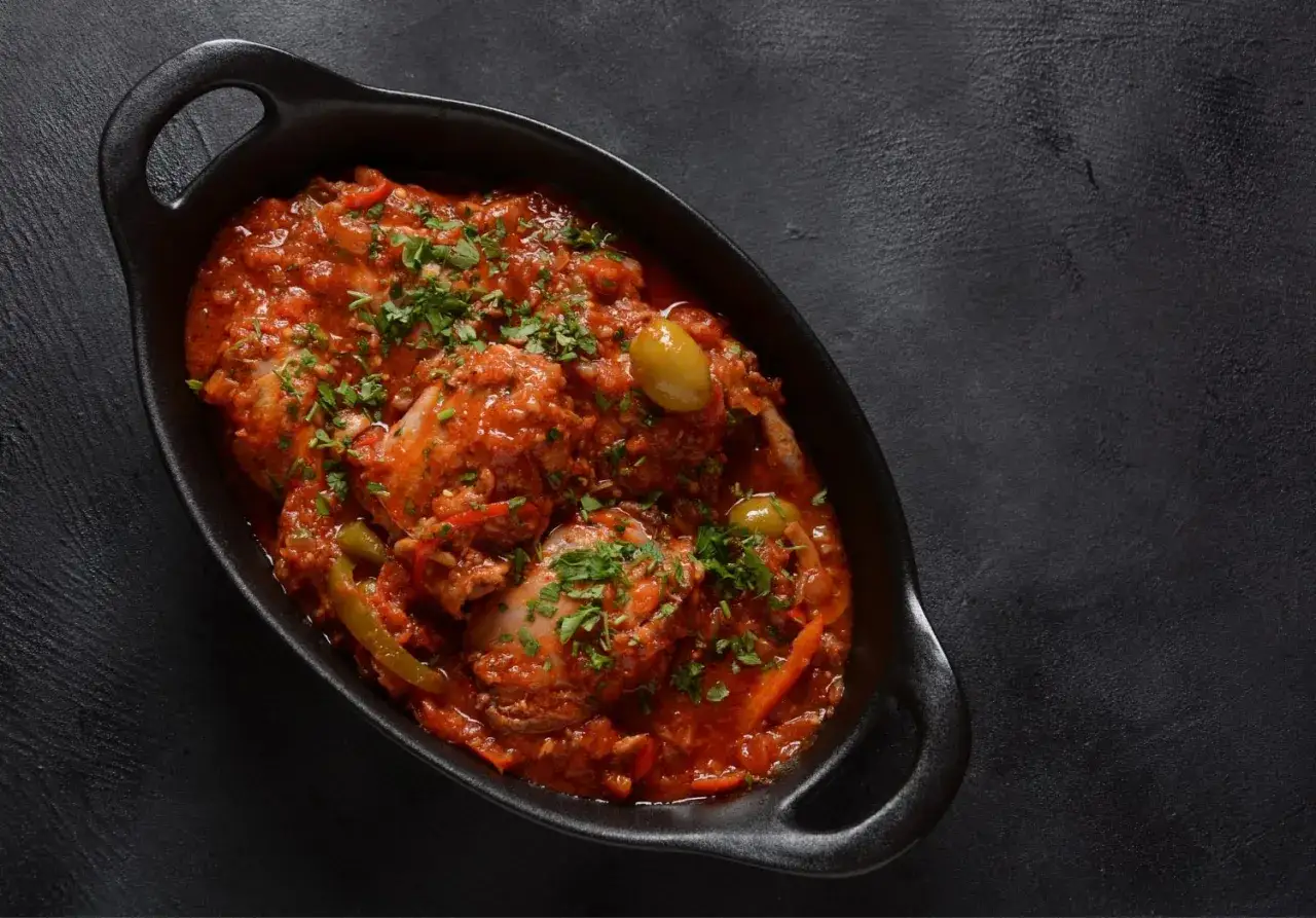 Pollo alla cacciatora in una cocotte nera, con pomodoro, olive e prezzemolo tritato. Un piatto tradizionale e saporito.