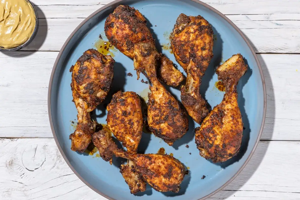 Cosce di pollo in friggitrice ad aria, dorate e speziate, servite su un piatto blu. Un contorno di senape gialla completa il piatto.