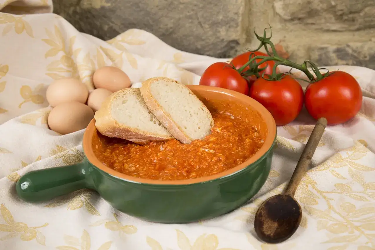 Uova al pomodoro in una ciotola verde, con pane fresco, pomodori maturi e uova crude.