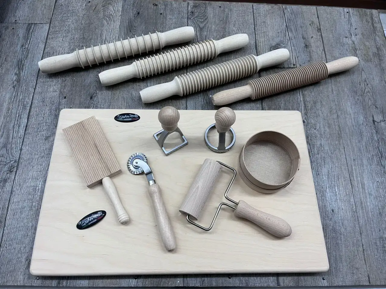 Set di attrezzi in legno per pasta fatta in casa: rotelle, rulli rigati, tagliapasta e setaccio.