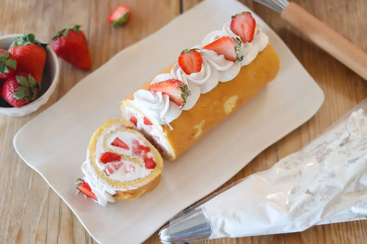 Rotolo panna e fragole decorato con panna montata e fragole fresche, pronto per essere gustato.