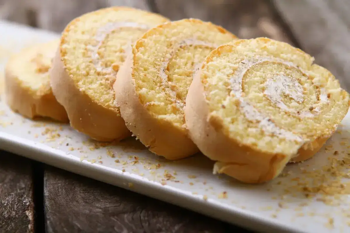 Fette di rotolo alla crema al latte, un dolce soffice e invitante, cosparse di briciole dorate su un piatto bianco.