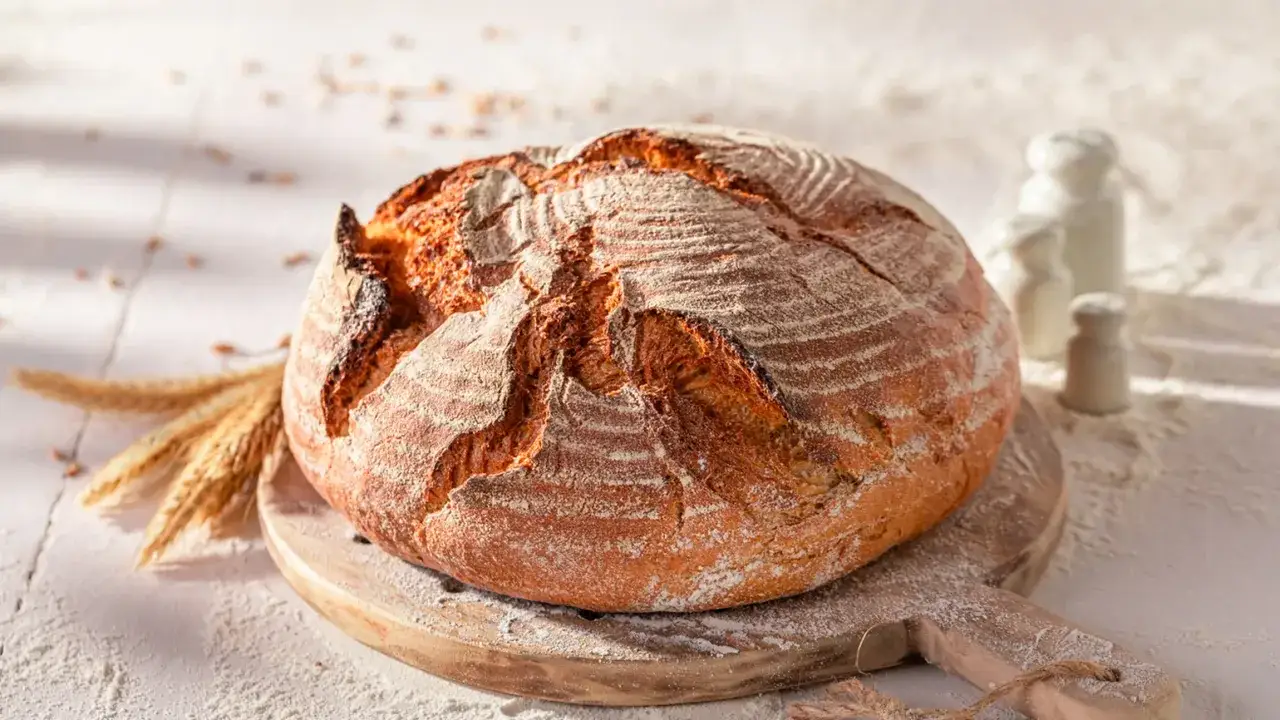 Pane croccante appena sfornato nella friggitrice ad aria, con spighe di grano e farina sparsa.