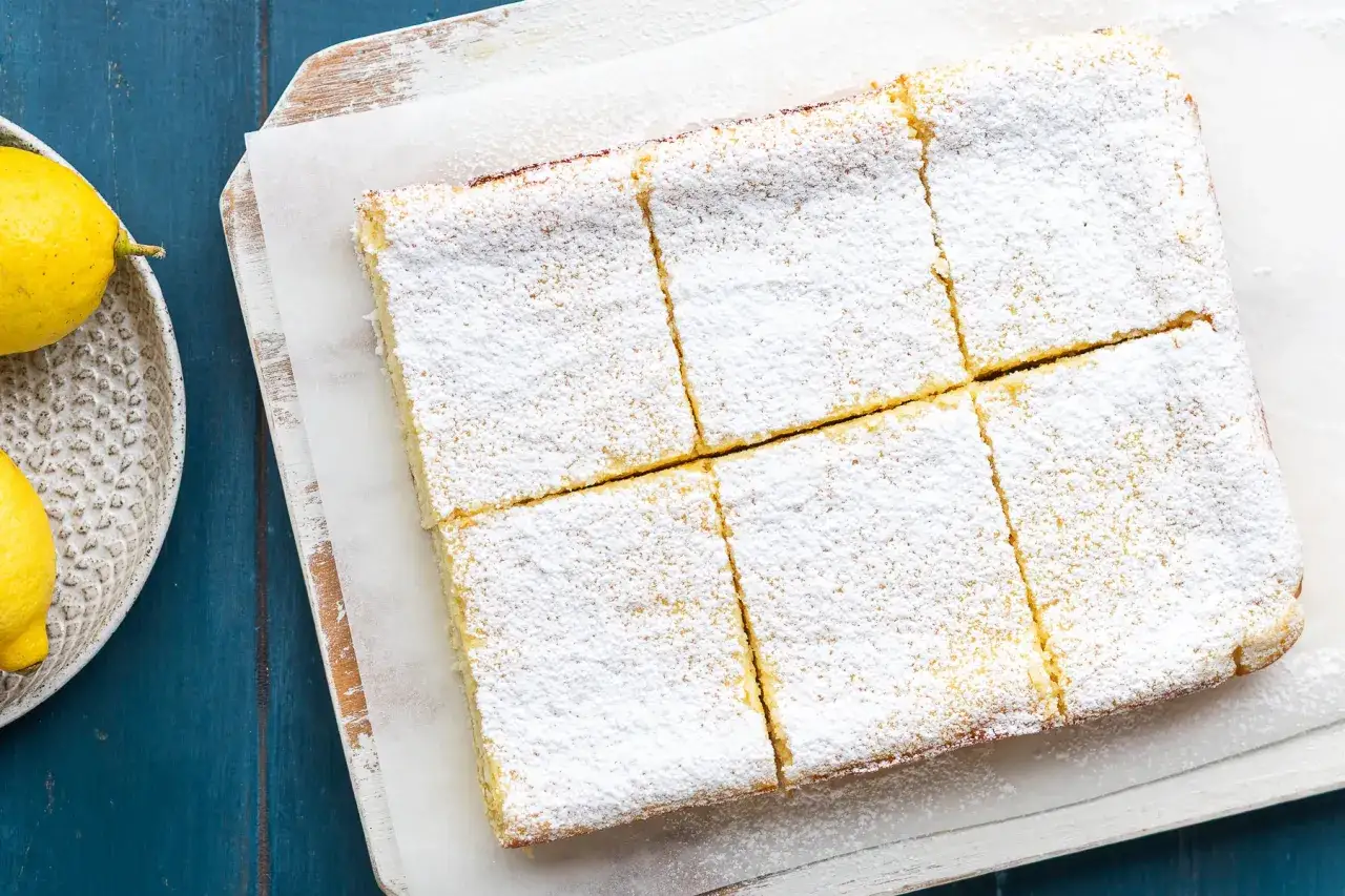 Una deliziosa torta delle monache, tagliata a quadrotti e cosparsa di zucchero a velo, accanto a limoni freschi.