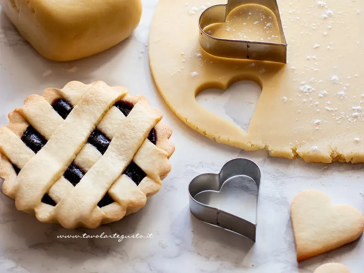 Preparazione di una crostata con pasta frolla classica: impasto, stampini a cuore e una deliziosa tortina già pronta.