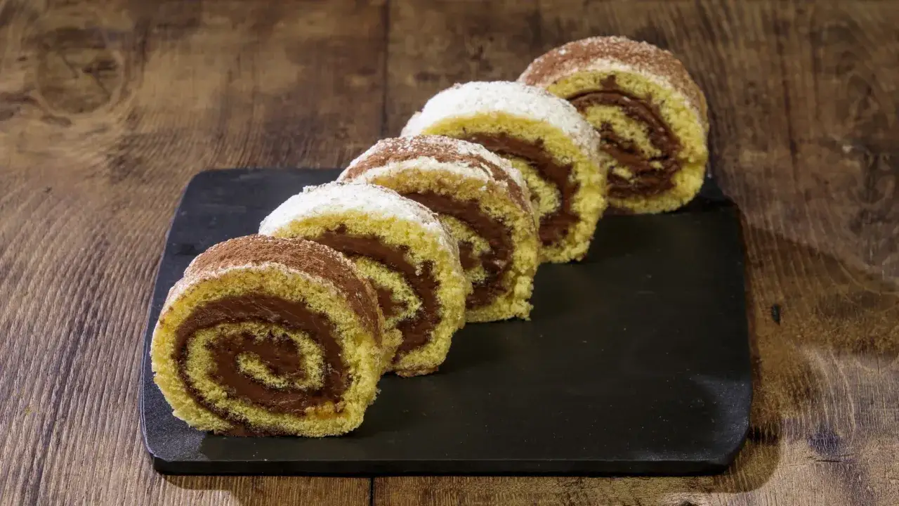 Fette di rotolo alla Nutella, spolverate di cacao e zucchero a velo, su una lavagna scura.