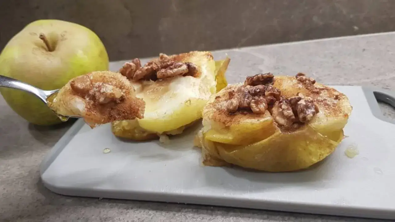 Mele cotte in friggitrice ad aria, dolci e profumate, con noci e cannella. Un cucchiaino mostra la morbidezza.