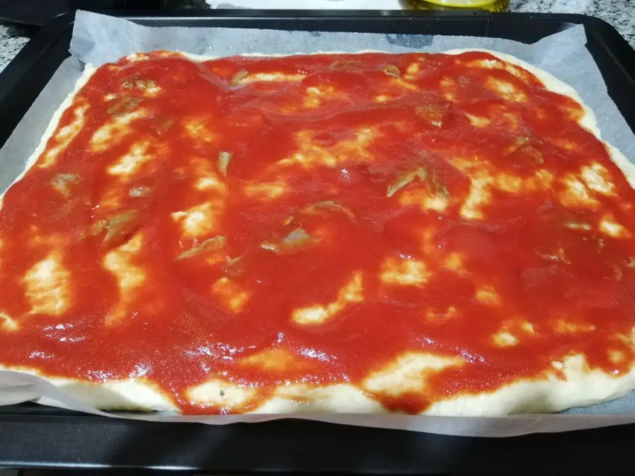 Pizza con lievito istantaneo, pronta per essere infornata. Base bianca coperta da salsa di pomodoro e pezzetti di mozzarella.