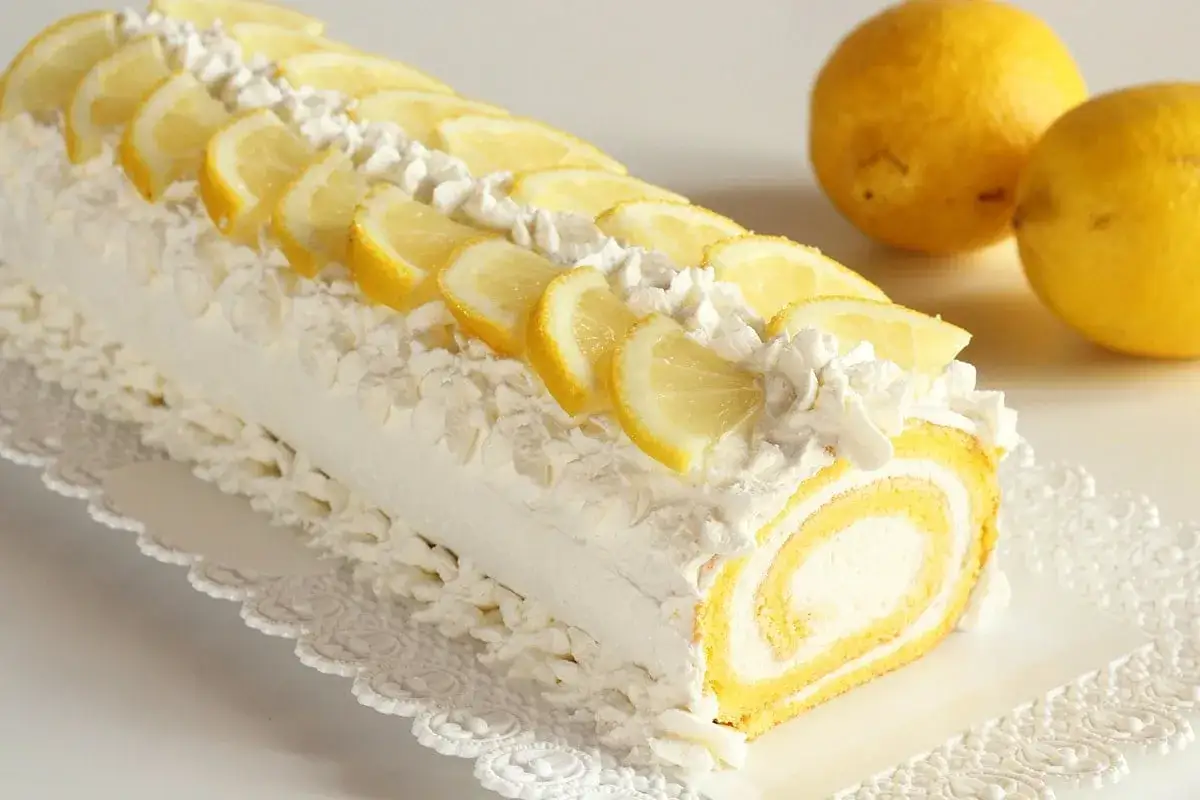 Rotolo soffice con crema al limone, decorato con panna montata e fettine di limone fresco. Un dolce estivo irresistibile.