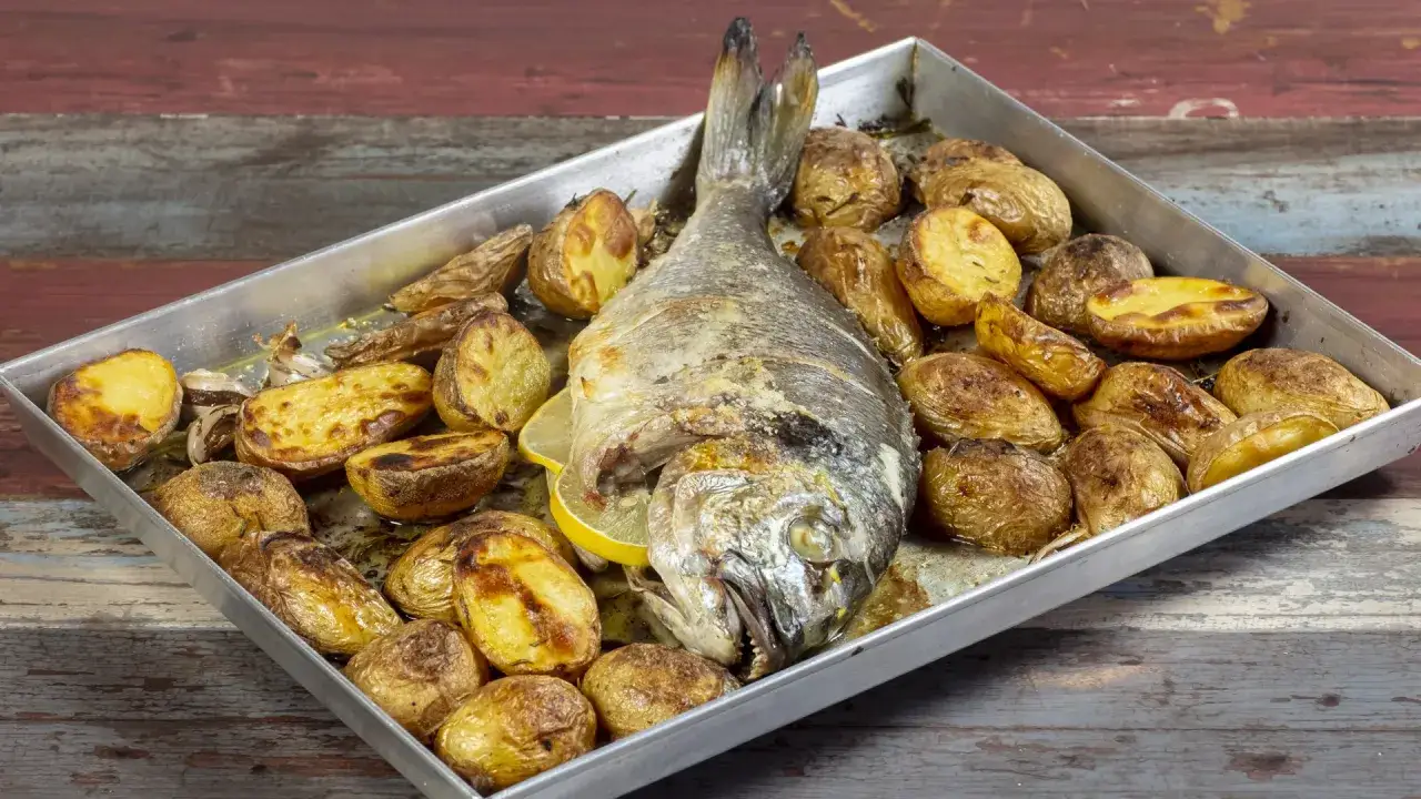 Orata al forno dorata e succulenta, circondata da patate arrosto croccanti e spicchi di limone.