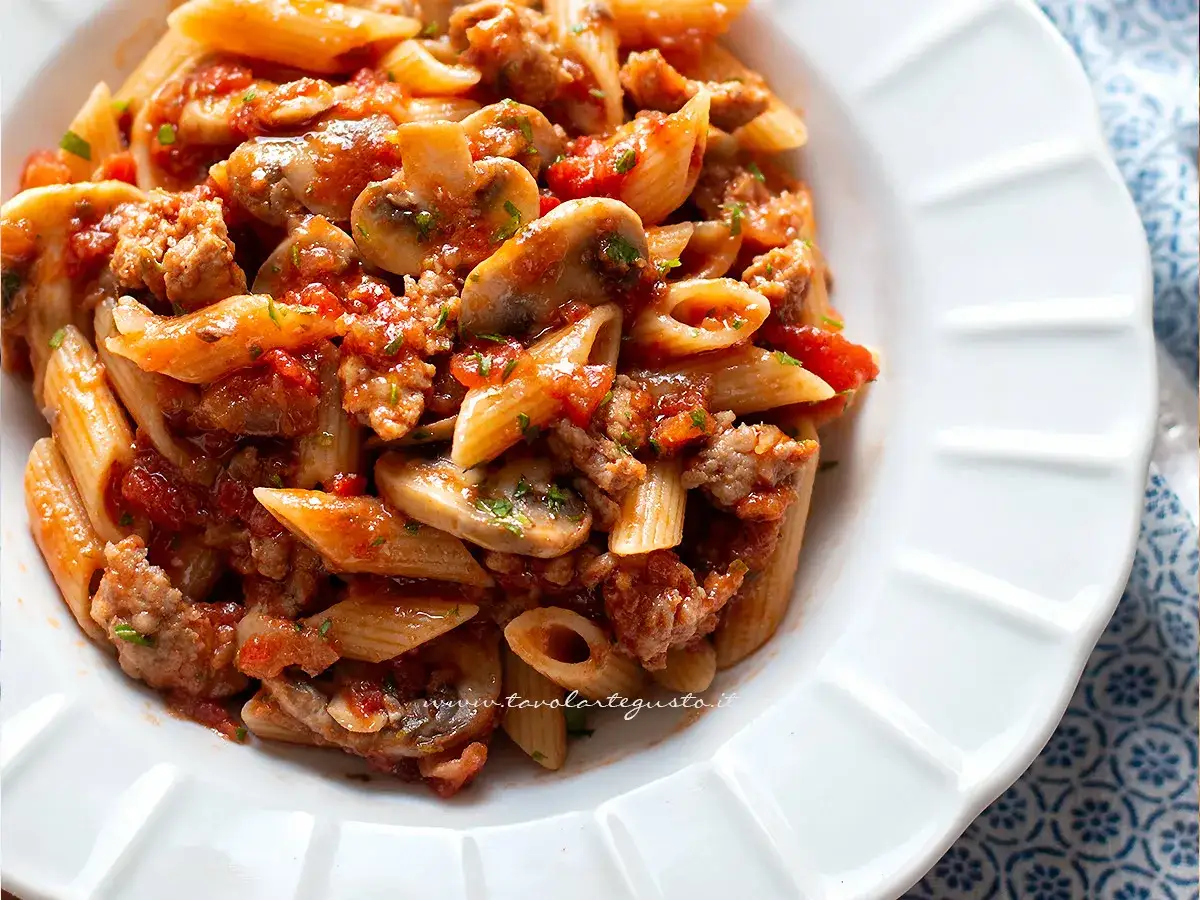 Piatto di pasta alla boscaiola con penne, funghi, salsiccia e pomodoro, condita con prezzemolo fresco.