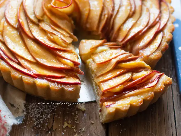 Una fetta di crostata di mele dorata, con mele caramellate disposte a spirale su una base friabile.