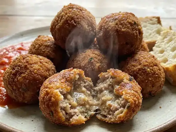 Polpette al forno dorate e croccanti, una aperta rivela un interno succulento. Servite con salsa rossa e pane.