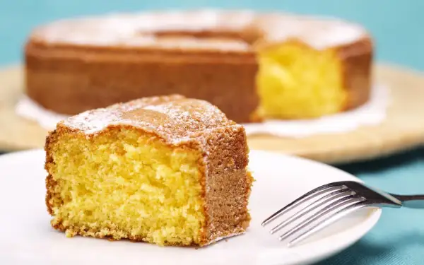 Una fetta di torta 7 vasetti soffice e dorata, spolverata di zucchero a velo, su un piatto bianco con una forchetta.