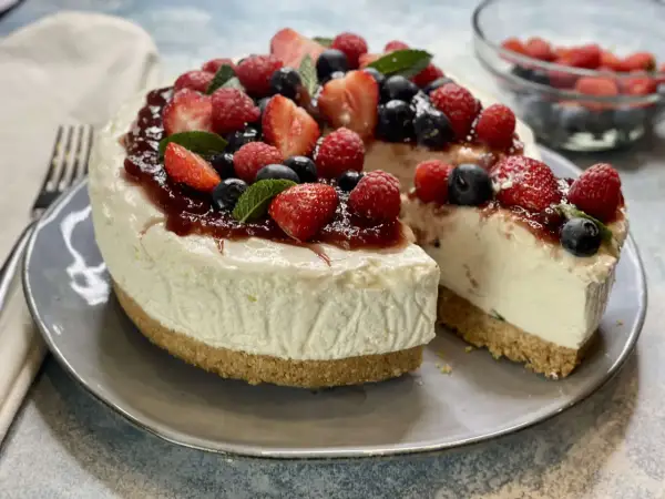 Deliziosa torta fredda allo yogurt, guarnita con fragole, lamponi, mirtilli e una cascata di marmellata. Perfetta per un dessert estivo.