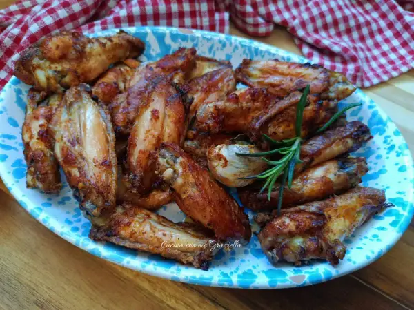 Alette di pollo al forno dorate e succulente, servite su un piatto decorato con un rametto di rosmarino.