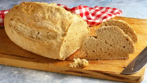 Pane casereccio con lievito istantaneo, tagliato su un tagliere di legno, con un tovagliolo a quadri rossi e bianchi.