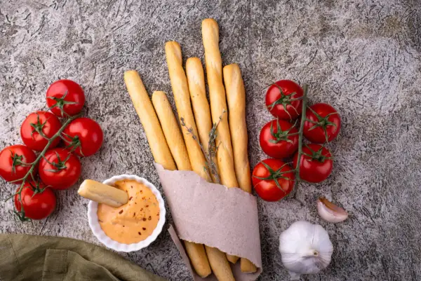 Grissini fatti in casa dorati, con pomodorini freschi, aglio e una salsa cremosa. Perfetti per un aperitivo rustico.