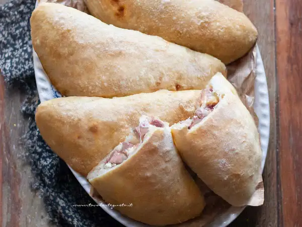 Calzoni al forno dorati e fragranti, ripieni di prosciutto e formaggio filante, pronti per essere gustati.