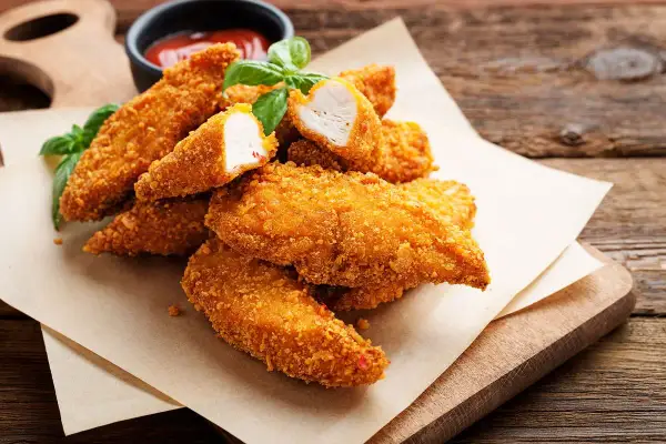 Bocconcini di pollo in friggitrice ad aria, dorati e croccanti, serviti con basilico fresco e salsa.