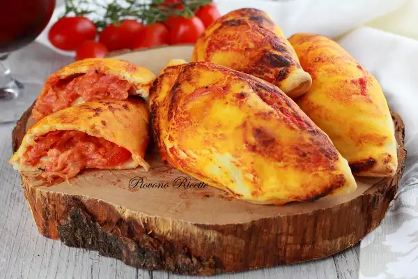 Panzerotti al forno dorati e ripieni di pomodoro e formaggio filante, serviti su un tagliere di legno.