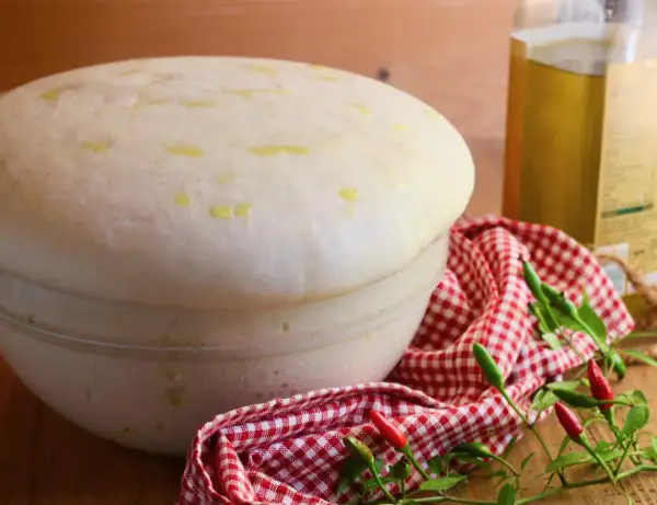 Impasto lievitato per pizza con lievito di birra, pronto per essere infornato. Olio d'oliva e peperoncini completano la scena.