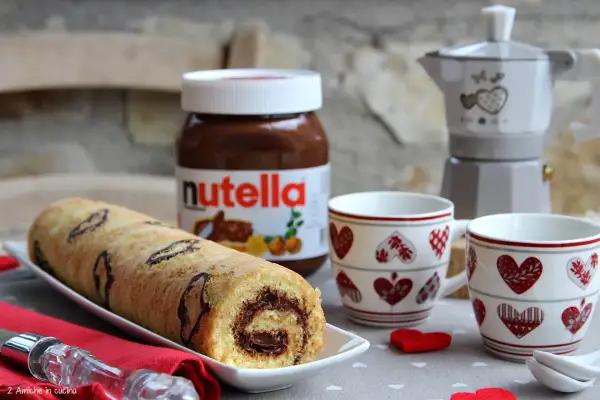 Rotolo alla Nutella pronto per essere gustato, con una moka e due tazze a tema cuore.