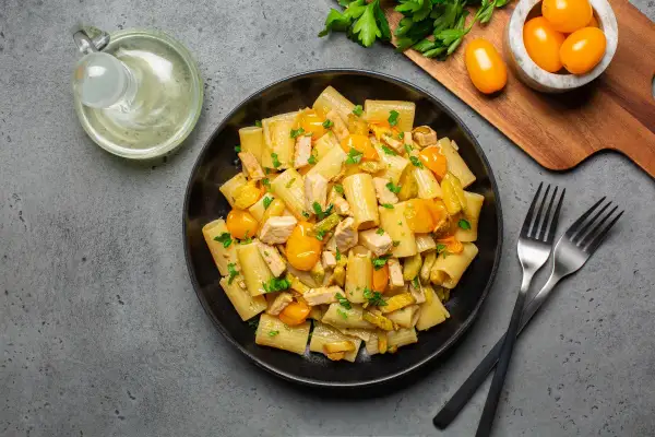 Piatto di pasta con pesce spada, pomodorini gialli e zucchine, guarnito con prezzemolo fresco.