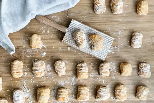 Gnocchi di zucca fatti in casa, pronti per essere cotti, sparsi su un tagliere di legno con un rigagnocchi.