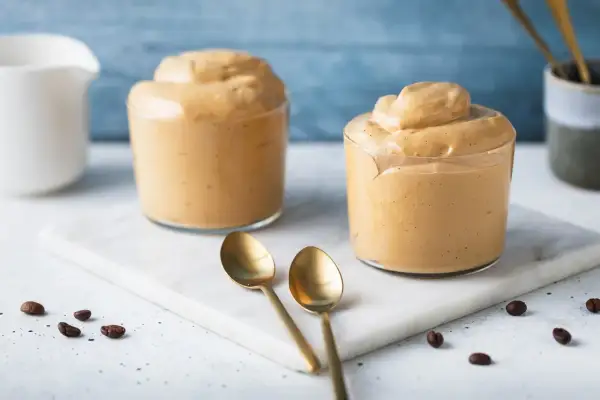 Due bicchieri di cremosa crema di caffè senza panna, perfetti per una pausa golosa. Chicchi di caffè e cucchiaini dorati completano la scena.