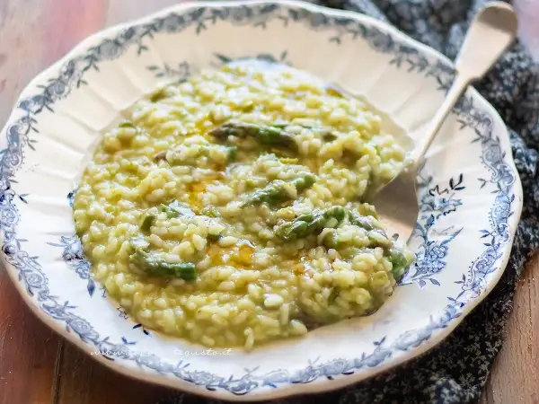 Un cremoso risotto con asparagi, servito su un piatto decorato. Un piatto primaverile che profuma di buono.