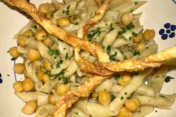 Piatto di ciceri e tria, pasta fresca con ceci e croccanti sfoglie fritte, guarnito con prezzemolo tritato.
