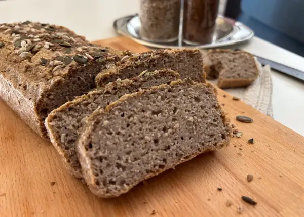 Fetta di pane di grano saraceno, cosparso di semi, su tagliere di legno.