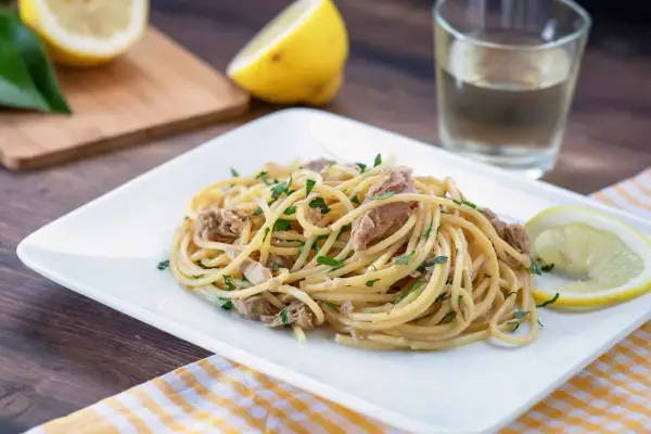 Un piatto di pasta tonno e limone, guarnito con prezzemolo fresco e spicchi di limone, pronto per essere gustato.
