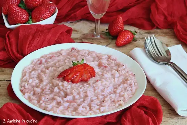 Un cremoso risotto alle fragole, guarnito con una fragola fresca, su un piatto bianco, circondato da fragole rosse e un drappo di seta.