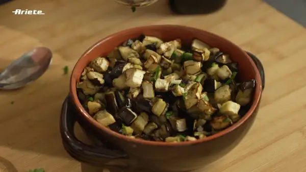 Melanzane in friggitrice ad aria, tagliate a cubetti e condite con erbe aromatiche, servite in una ciotola di terracotta.