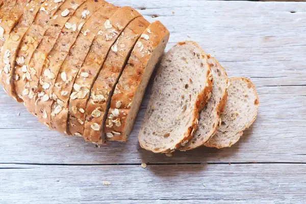 Pane fatto in casa ricetta della nonna, con crosta dorata e semi, affettato su un tavolo di legno.