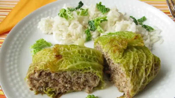 Involtini di verza ripieni di carne e riso, serviti su un piatto bianco con contorno di riso bianco e foglie di verza sminuzzate.