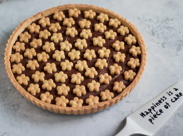 Deliziosa crostata alla nutella con decorazioni a forma di fiorellini. Un dolce che porta gioia, come dice la spatola: "Happiness is a piece of cake".