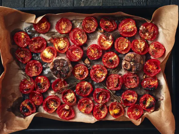 Pomodorini al forno, caramellati e profumati al rosmarino, con teste d'aglio arrostite.