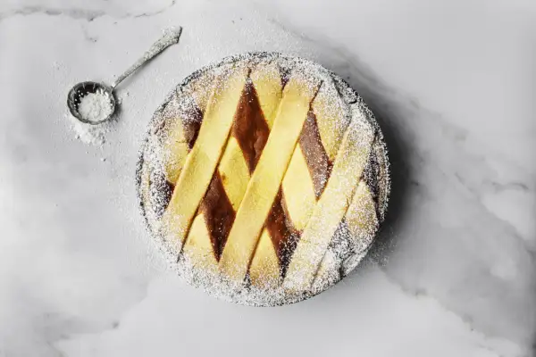 Pastiera napoletana pronta, cosparsa di zucchero a velo. Un assaggio di come si fa la pastiera, con la sua crostata decorata a rombi.