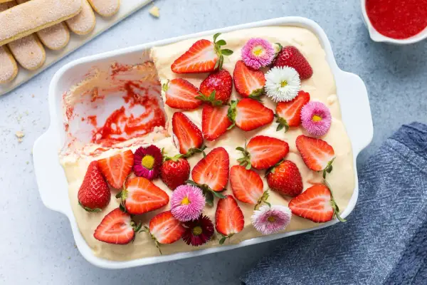Tiramisù alle fragole ricetta originale: un dolce fresco e goloso, decorato con fragole fresche e piccoli fiori colorati.